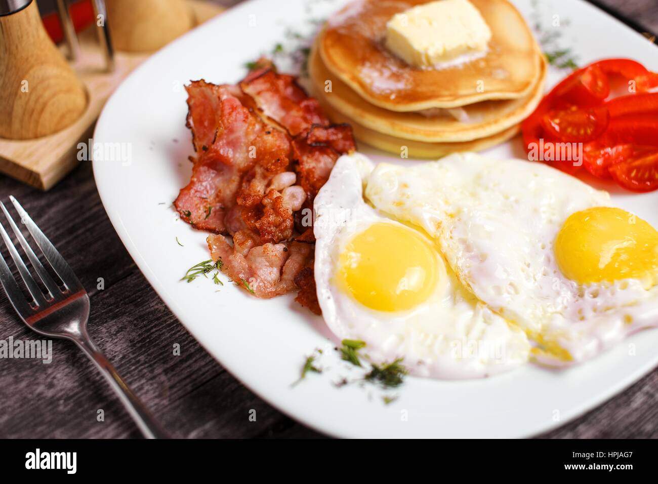 Tasty breakfast with fried eggs, pancakes, bacon and vegetables. Stock Photo