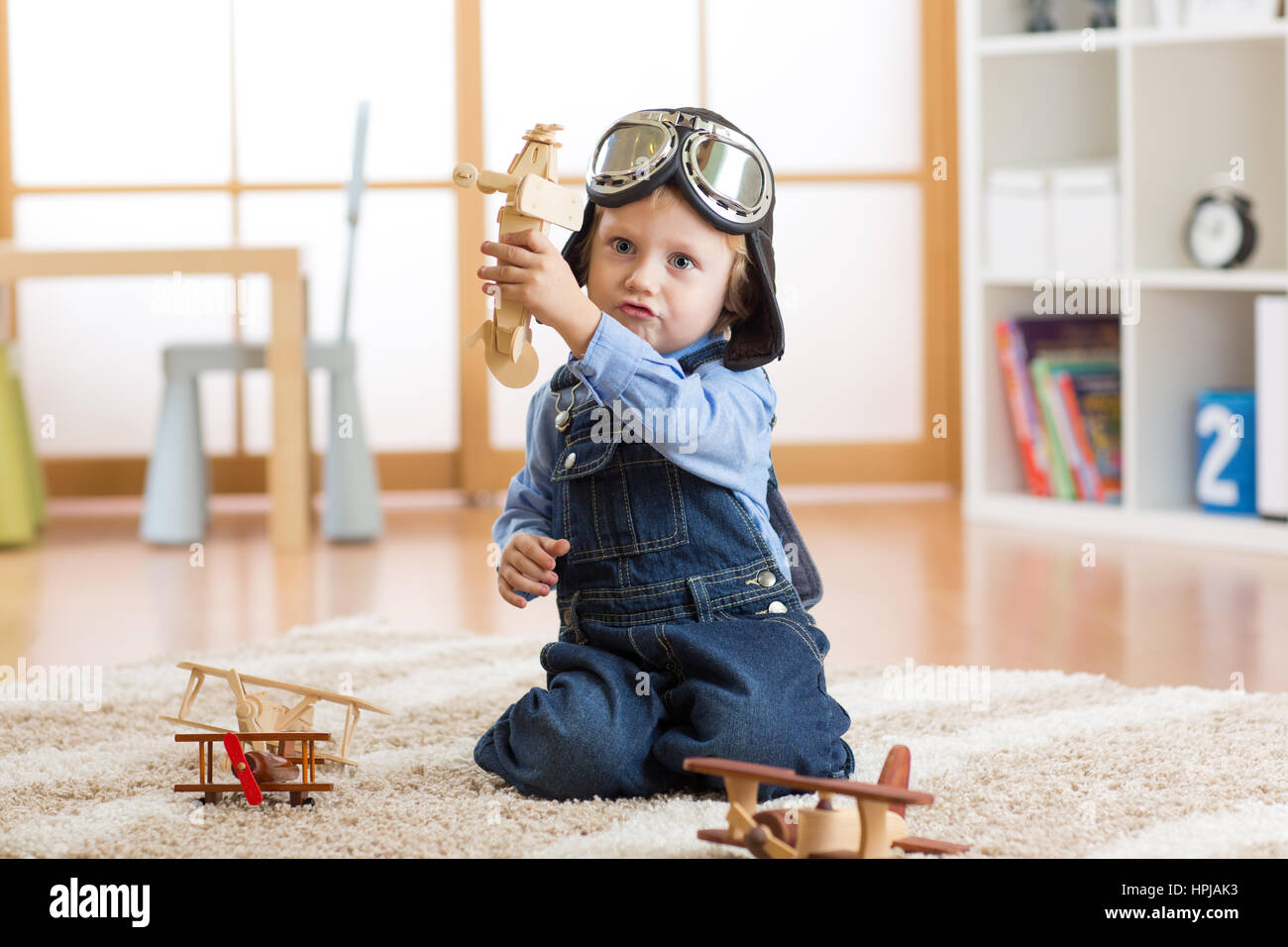 Pilot aviator child plays with wooden toy airplanes on floor in his room Stock Photo