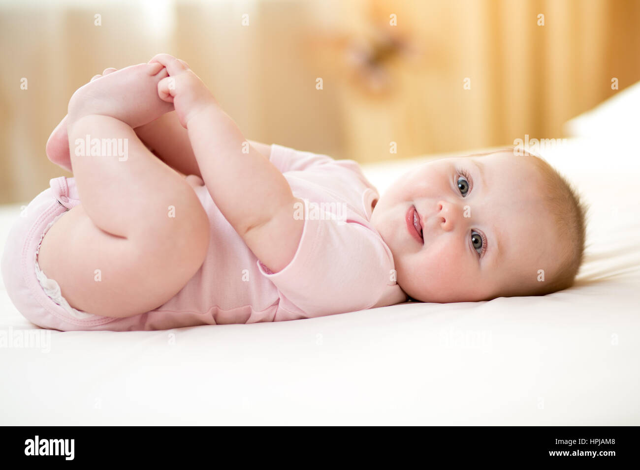 Funny smiling baby infant girl playing with her feet Stock Photo