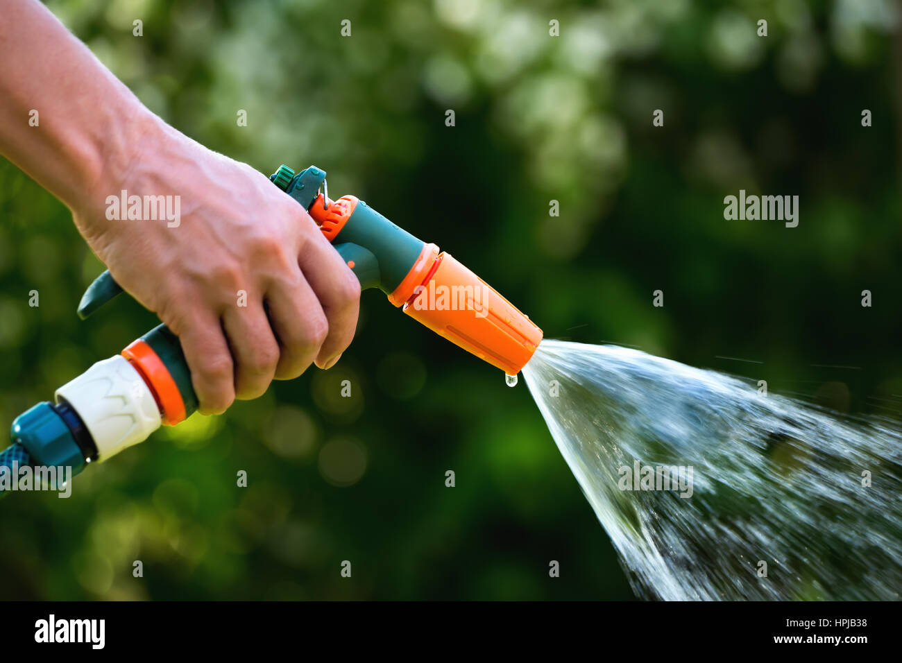 Gun water hose nozzle sprayer. Woman hand holding  hose sprayer head watering garden. Shallow depth of field Stock Photo