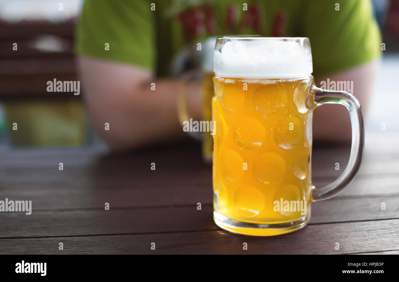 Glass of tapped craft beer. Unfiltered lager on a pub table. Man in background. Shallow depth of field Stock Photo