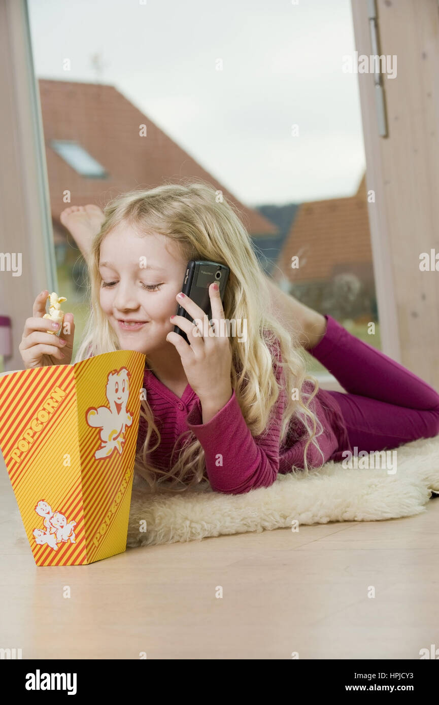 Model released , Maedchen telefoniert mit Handy und isst Popcorn - girl with mobile phone eats popcorn Stock Photo