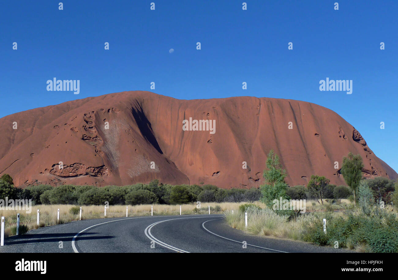 Ayers Rock contrasted by bright blue sky with the moon visible Stock ...