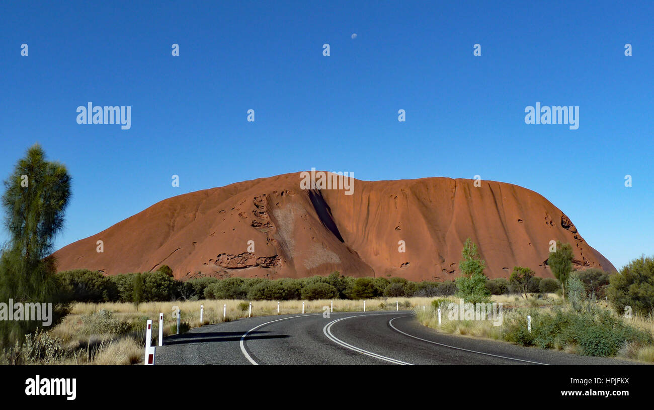 Ayers Rock contrasted by bright blue sky with the moon visible. Stock Photo