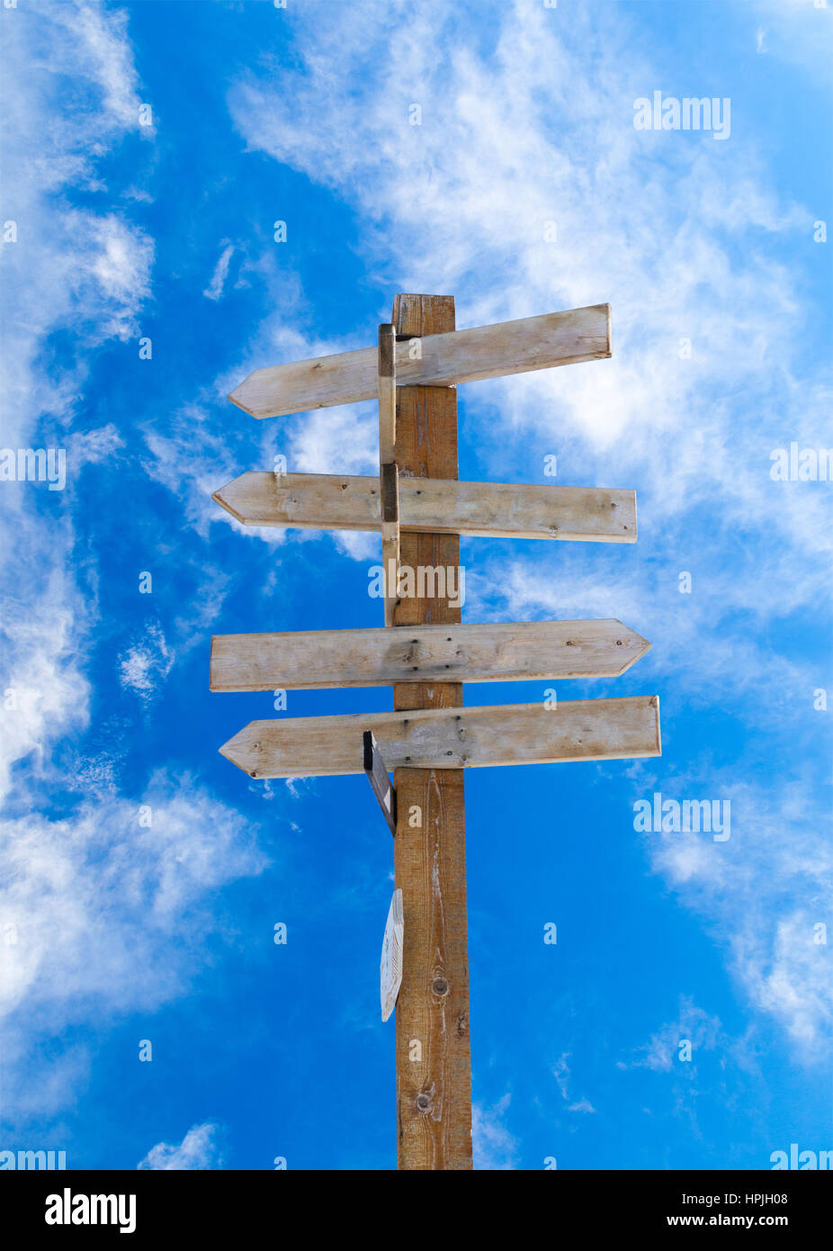 Old wooden arrow signpost against a blue cloudy sky with copy space. Idea of crossroads and concept of being lost, confused or indecisiveness. Vertica Stock Photo