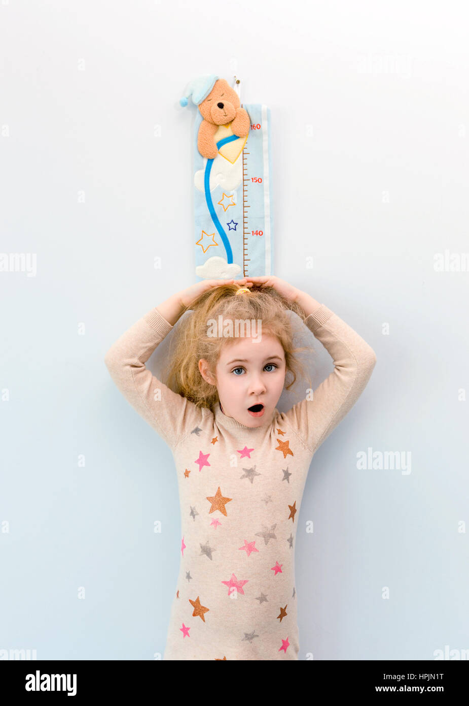 Little blonde girl measuring height against wall in room Stock Photo