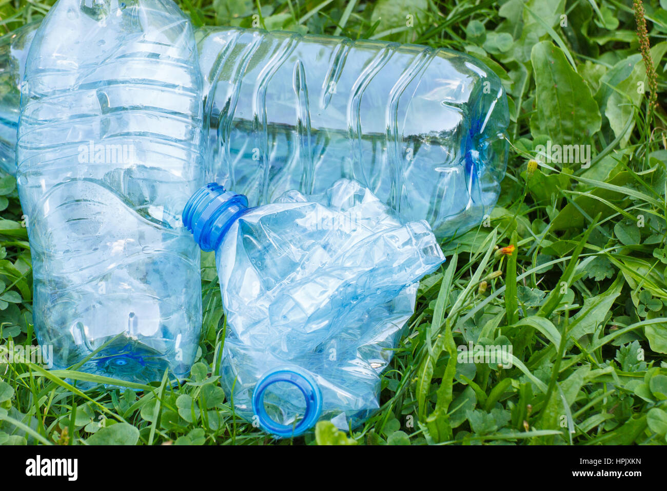 Crushed plastic bottles of mineral water on grass in park, concept of environmental protection