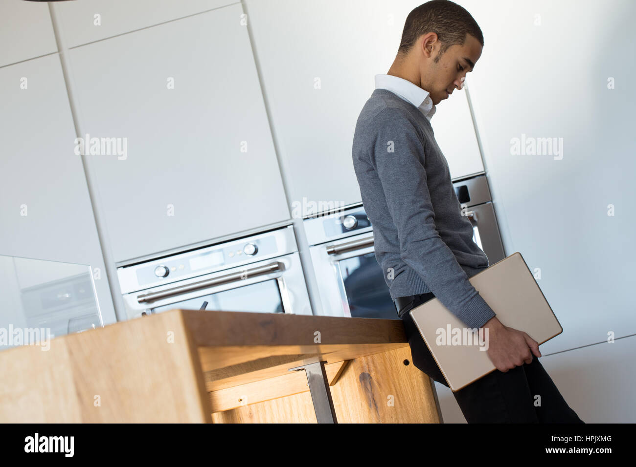 young handsome black business man in a kitchen holding a big digital tablet and thinking about the next move; concept of lifestyle of businessman Stock Photo