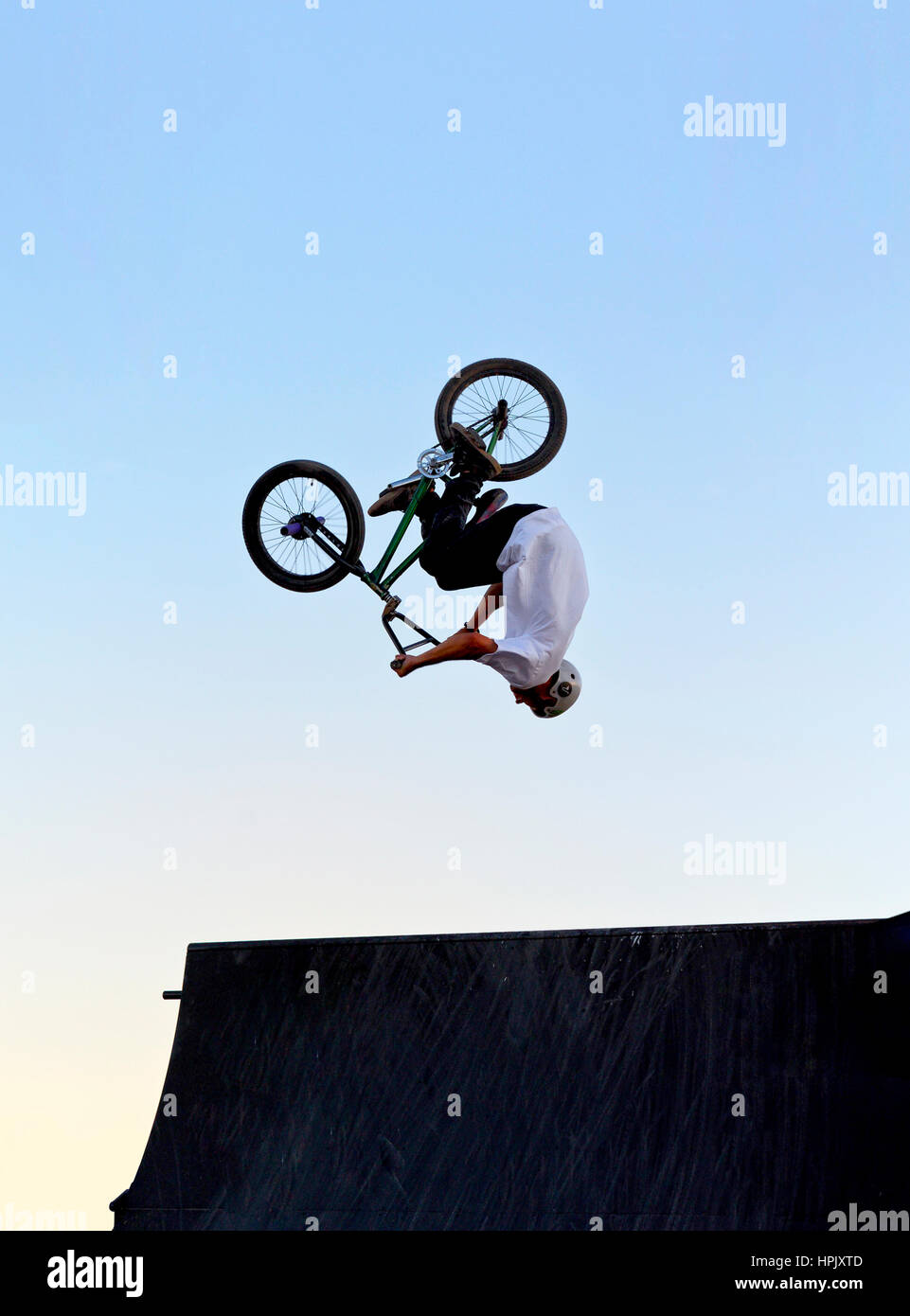 A person doing a back flip over a bike jump ramp on a BMX bicycle Stock