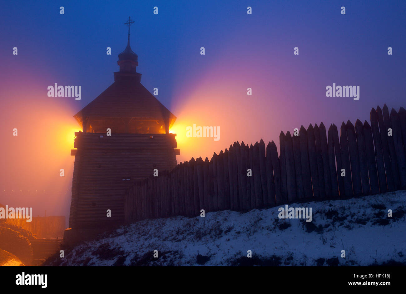 Wooden tower of cossacks fortress 'Zaporizhian Sich' in evening fog with rays of orange illumination lights, Khortytsia island, Zaporozhye, Ukraine Stock Photo