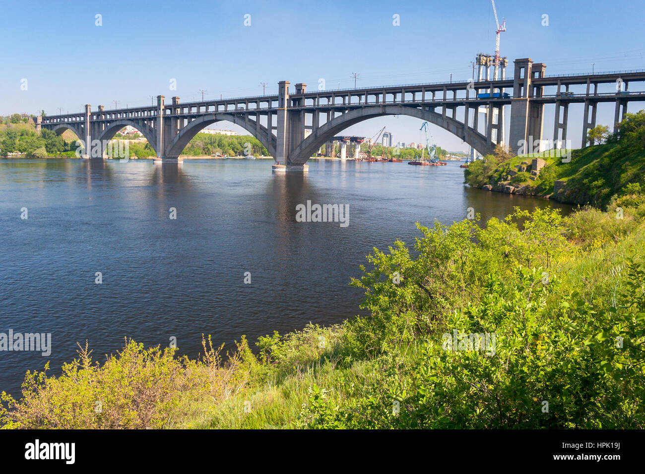 Preobrazhensky concrete arched bridge on Dnieper river in spring, view from Khortytsia island, Zaporozhye, Ukraine Stock Photo