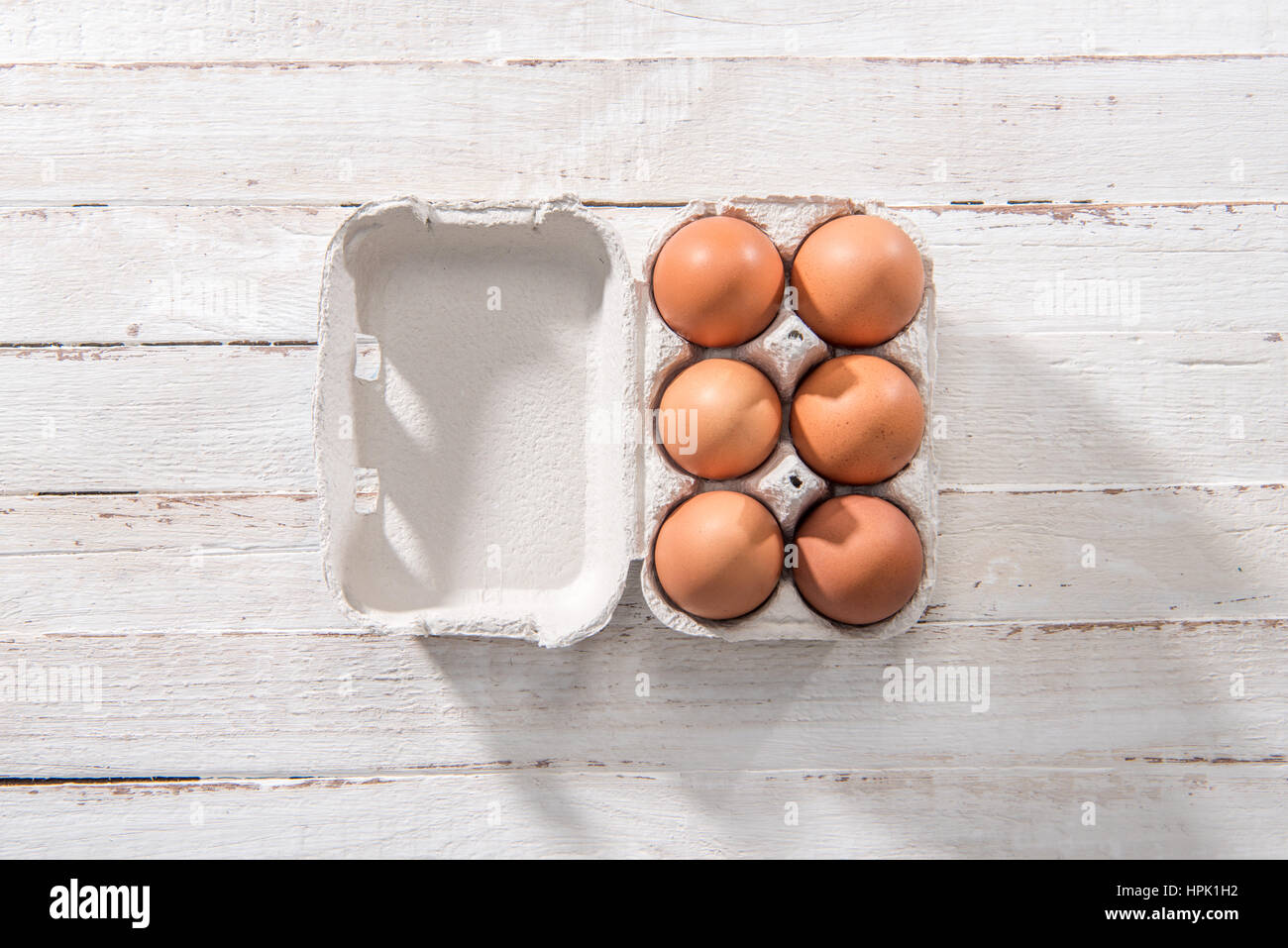 Top view of raw chicken eggs in open egg box on white wooden table ...