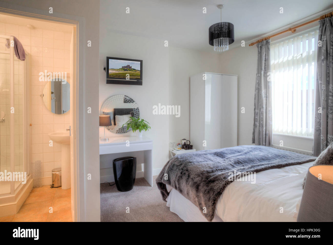Empty hotel room with a double bed. A bathroom can be seen in the other room through the door. Stock Photo