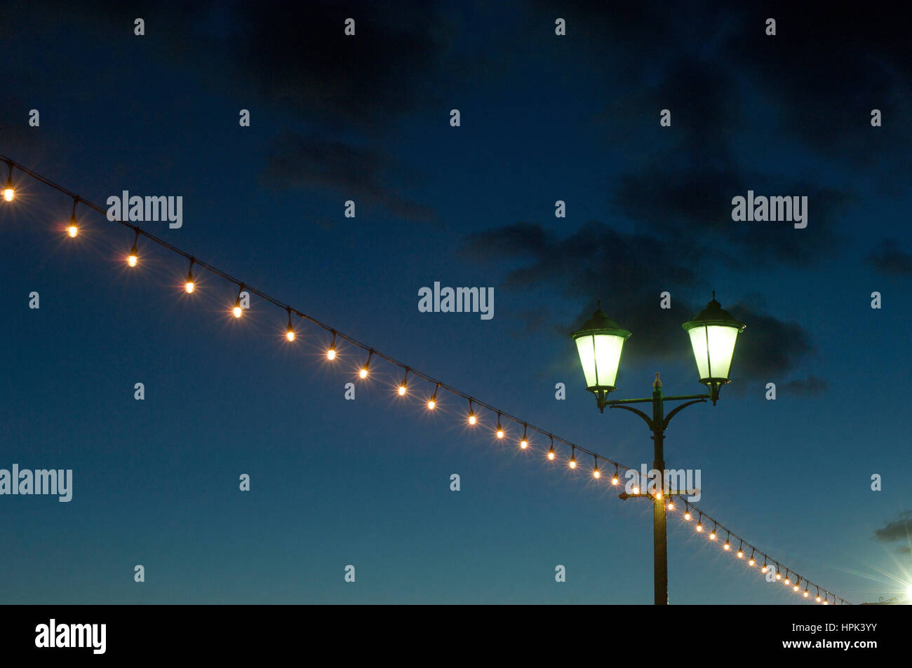 Street lamp and string of lights against darkening sky Stock Photo