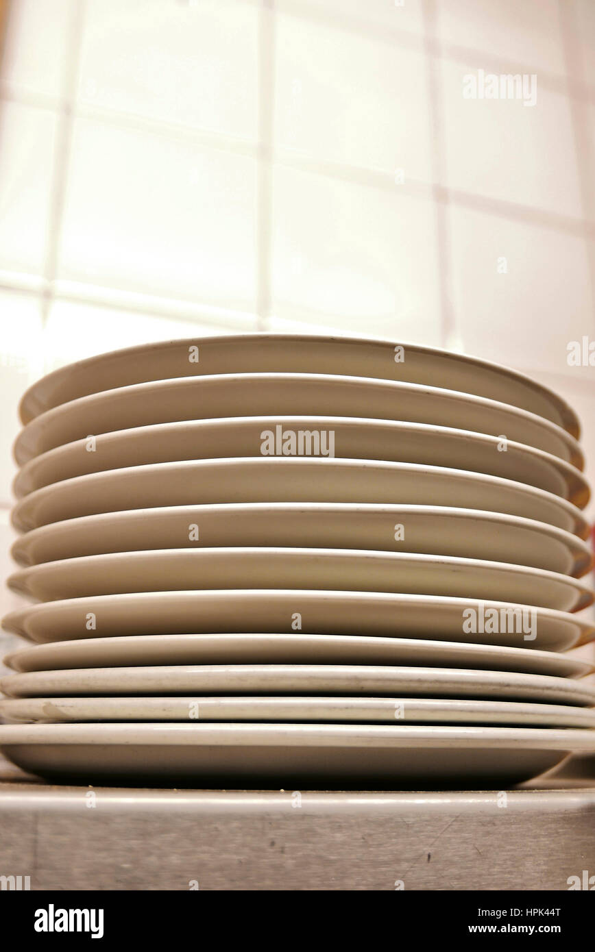 Stack of white plates in kitchen against tiled wall Stock Photo