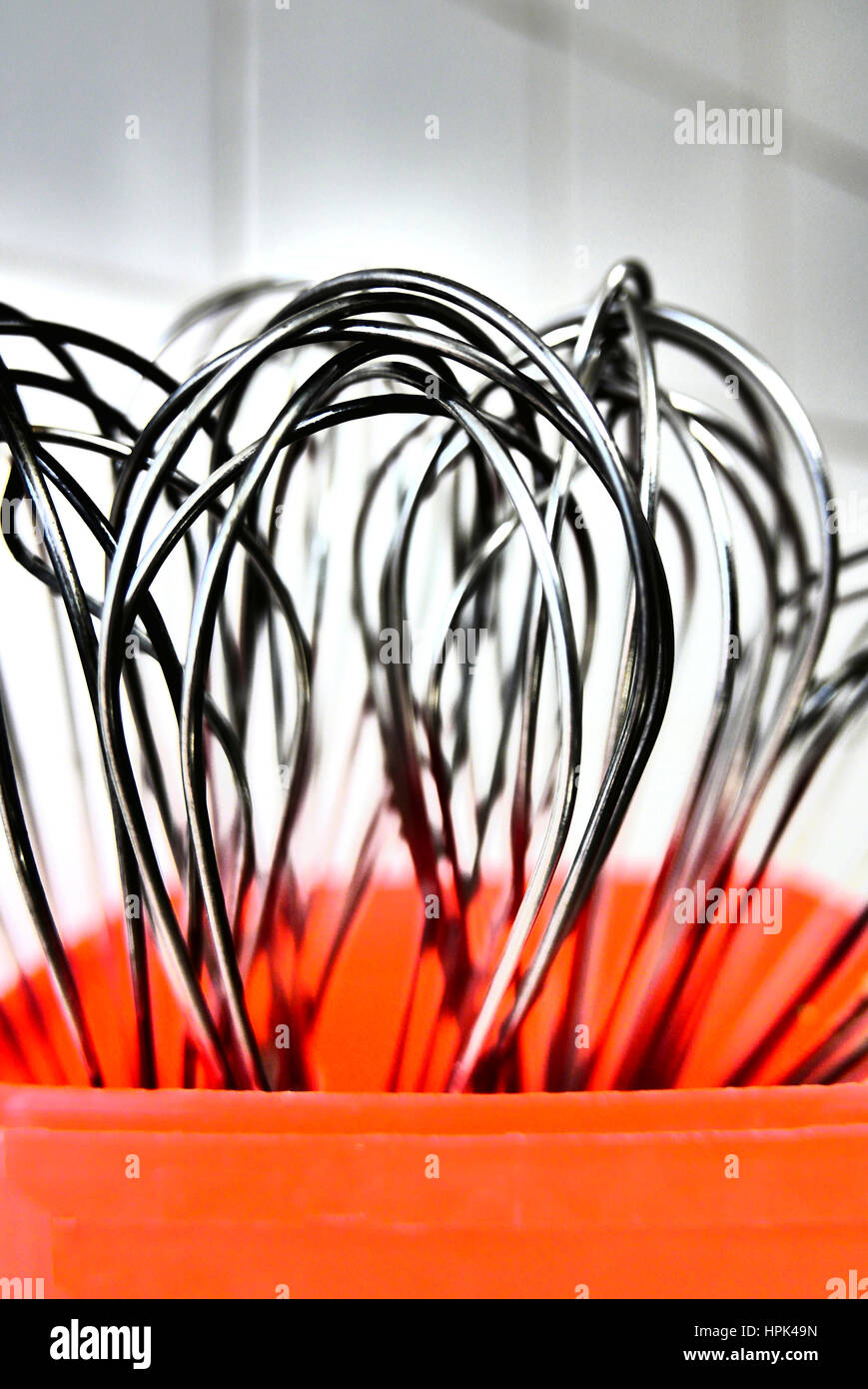 Metal food whisks in red plastic container against white tiled kitchen background Stock Photo