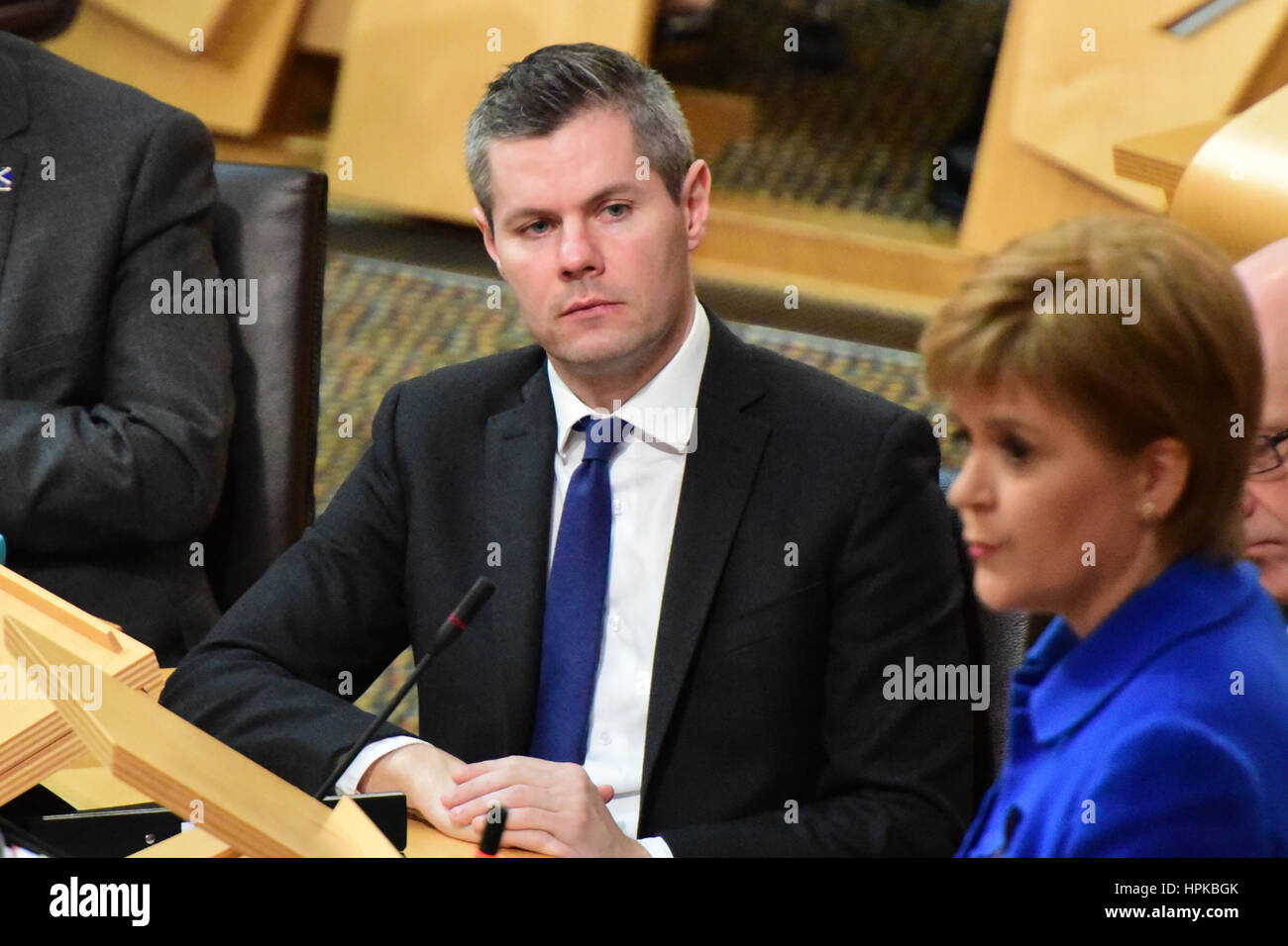 Edinburgh, Scotland, UK. 23rd February 2017. Finance Secretary Derek Mackay listens as Nicola Sturgeon speaks during First Minister's Questions in the Scottish Parliament, shortly before the Stage 3 (final reading) debate on the Scottish budget, Credit: Ken Jack/Alamy Live News Stock Photo