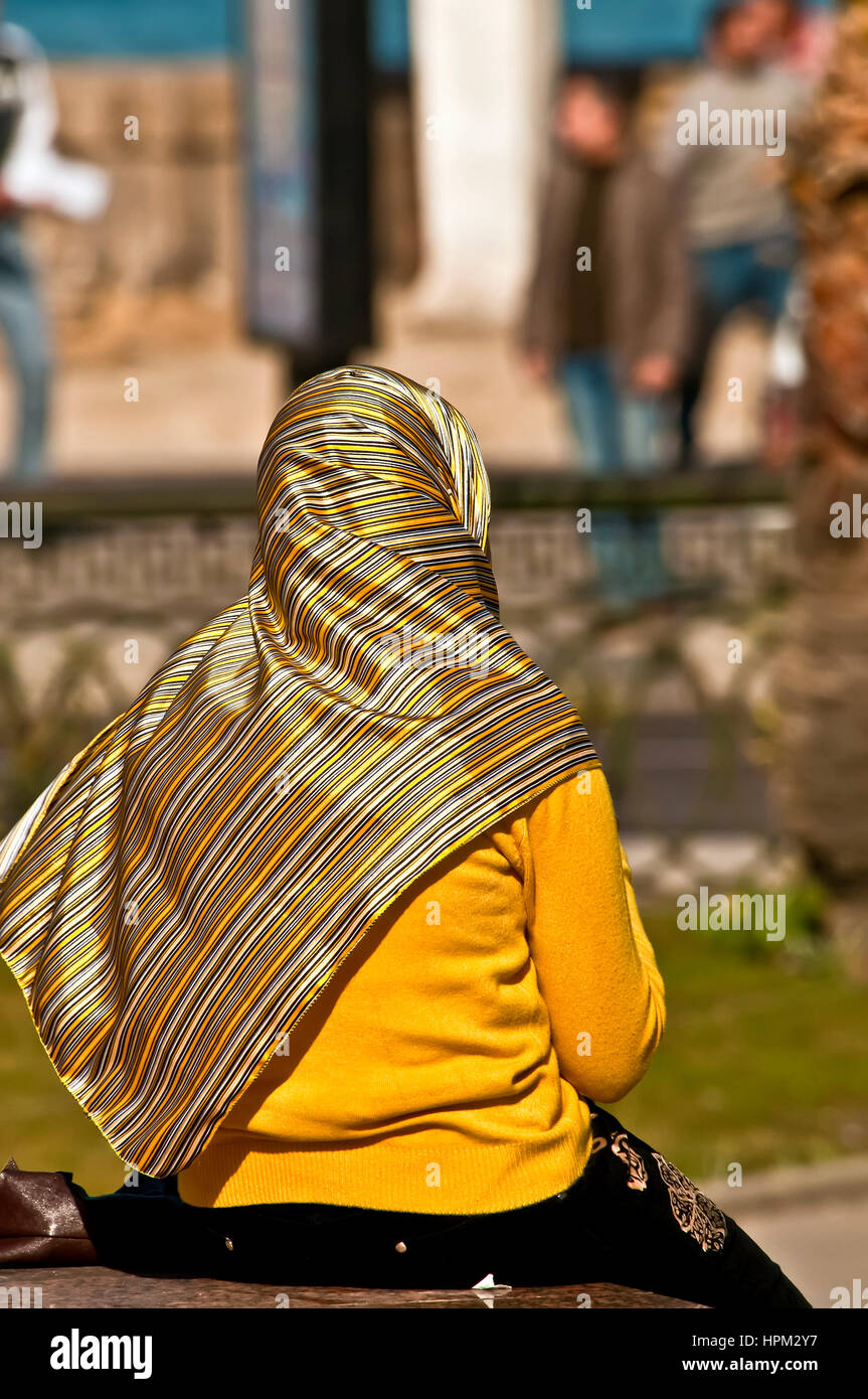 Muslim woman with bright yellow clothing sits alone by the corniche waterfront in Alexandria Stock Photo