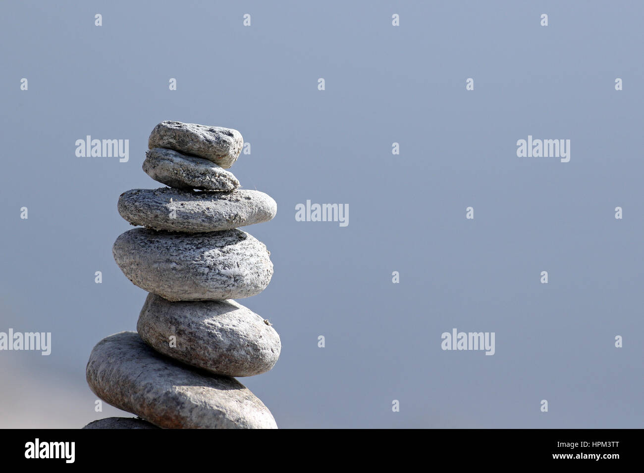 Column of hand piled granite zen stones against blue water background ...