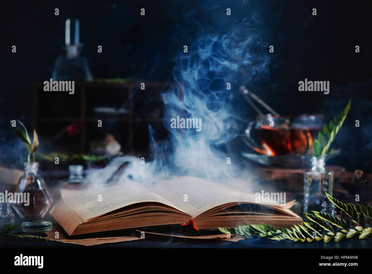 Still life with open spell book, magical smoke, herbs, witchcraft tools and tea Stock Photo