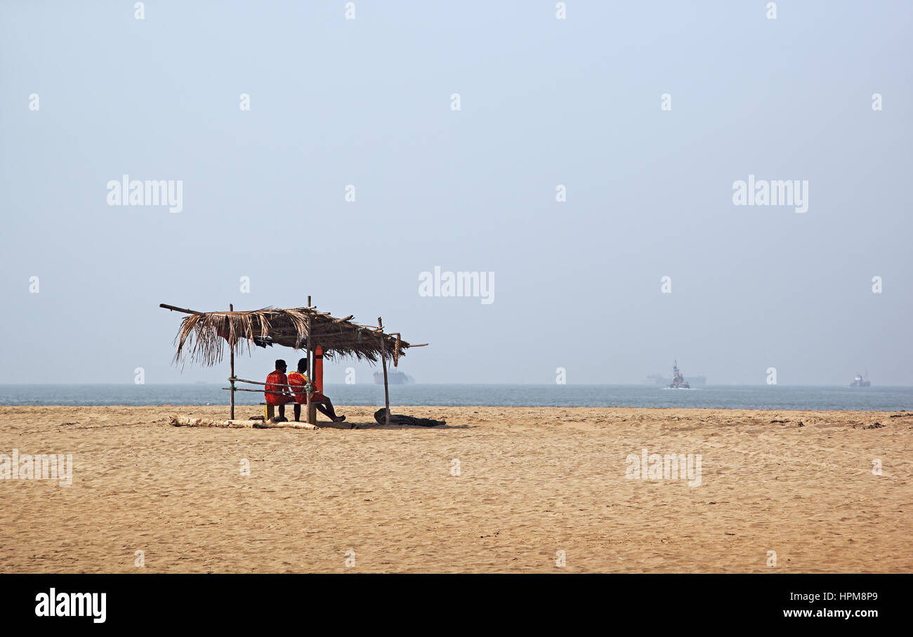 Two life guards keep vigil under a temporary thatched shed in Miramar Beach in Goa, India. Stock Photo