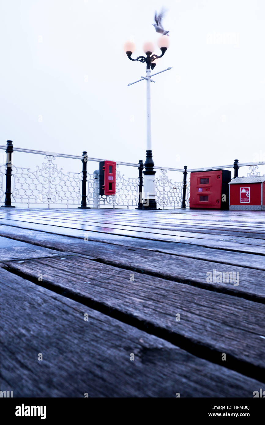 texture of wooden floor of the pier in the forefround with antique lamp post in the background red life belts on railing and a seagull with movement i Stock Photo
