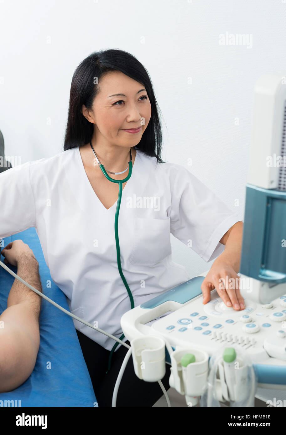 Smiling female doctor operating ultrasound machine while examining male patient in hospital Stock Photo