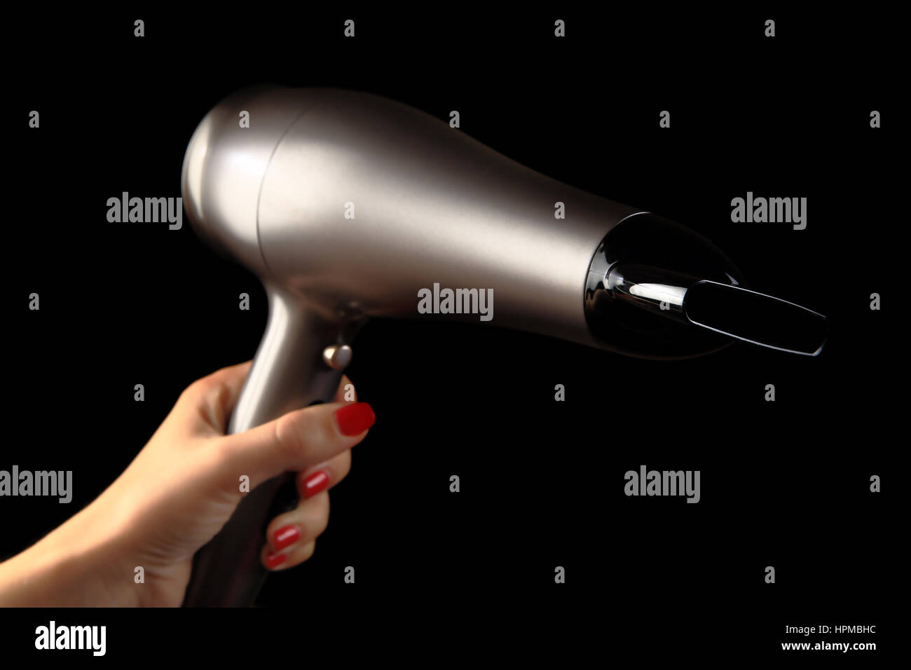 Hair dryer in  female hand. Black background. Hand with red painted nails Stock Photo