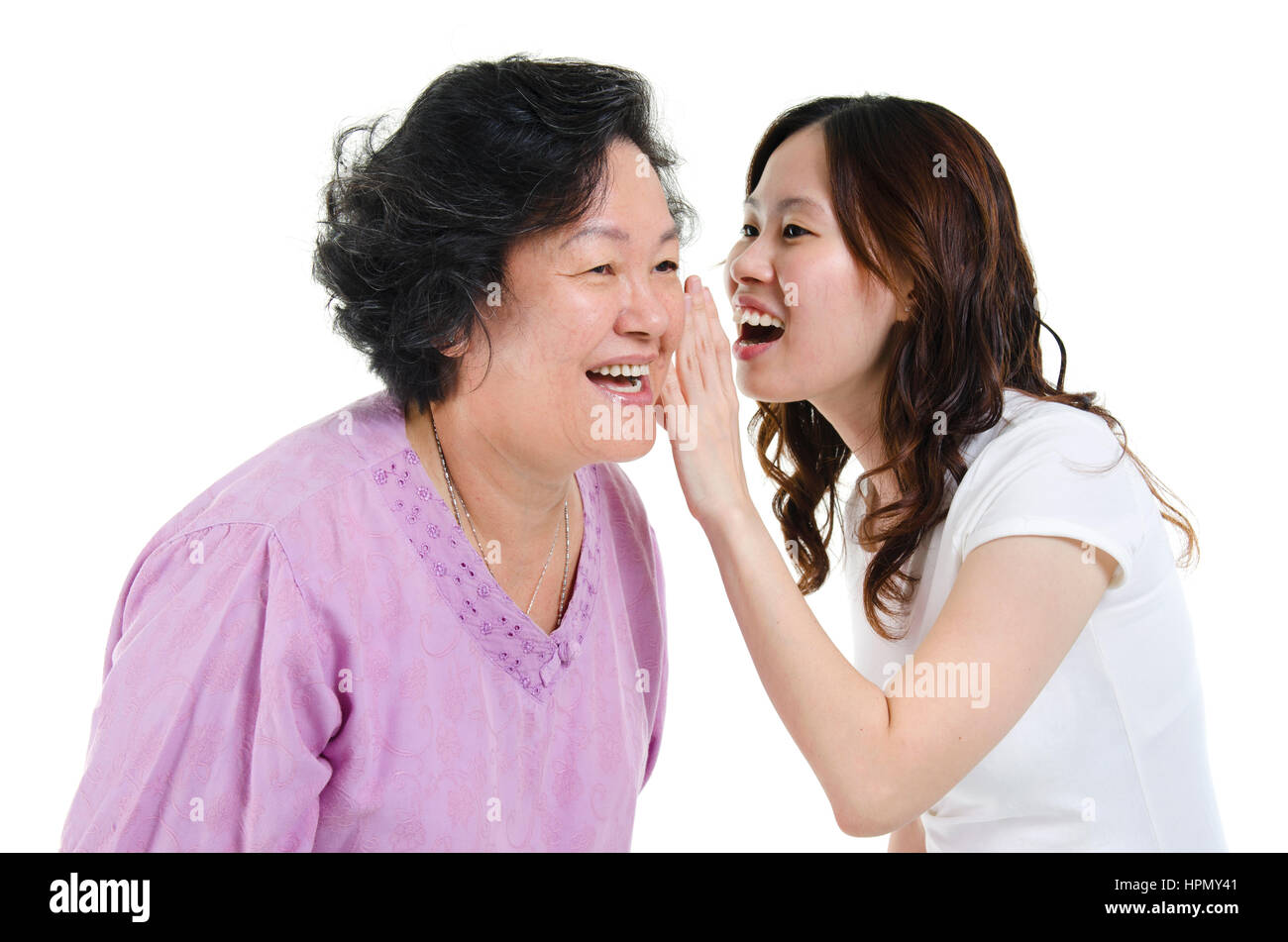 Portrait of Asian adult daughter sharing secrets to her senior mother, isolated on white background. Stock Photo