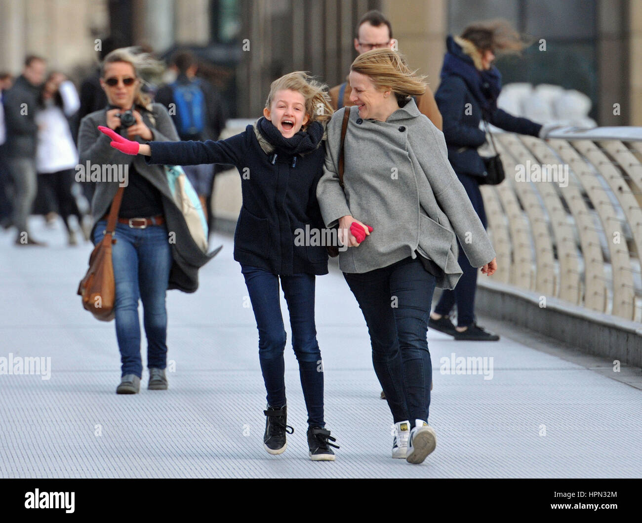 A young girl and a woman laugh as they are caught in a gust of wind as they walk across Millennium Bridge in central London, as flights have been cancelled and commuters were warned they faced delays after Storm Doris reached nearly 90mph on its way to batter Britain. Stock Photo