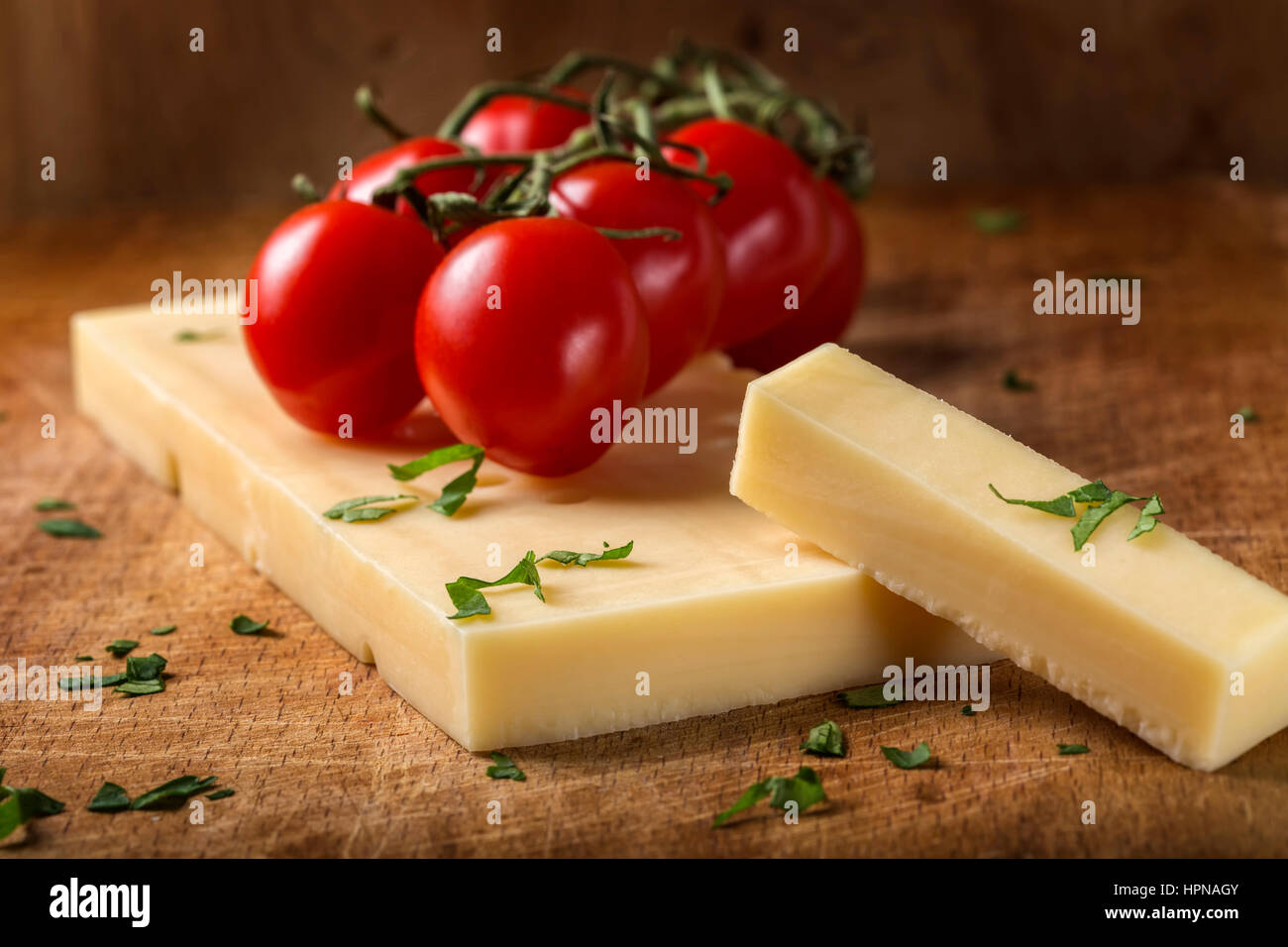 Emmental cheese with cherry tomatoes and herbs on wooden cutting board Stock Photo