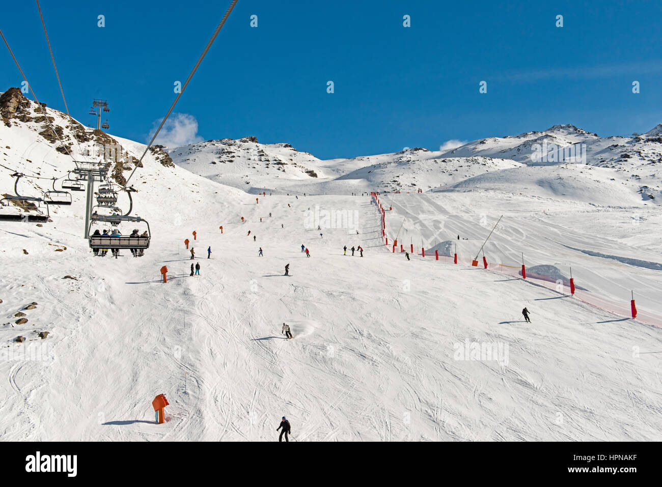 Skiers on a ski slope piste in winter alpine mountain resort with chairlift Stock Photo