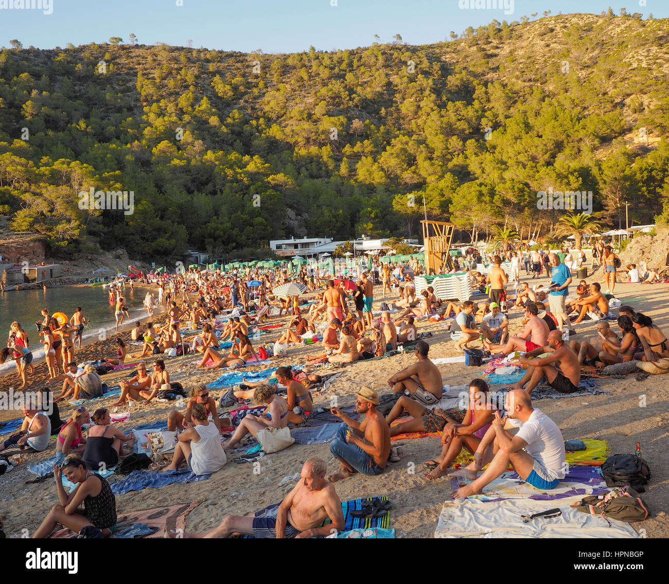 GATHERING OF VISITORS ON THE BEACH AT BENIRRAS BEACH IBIZA AND LISTENING TO DRUMS BEING PLAYED BY HIPPYS Stock Photo