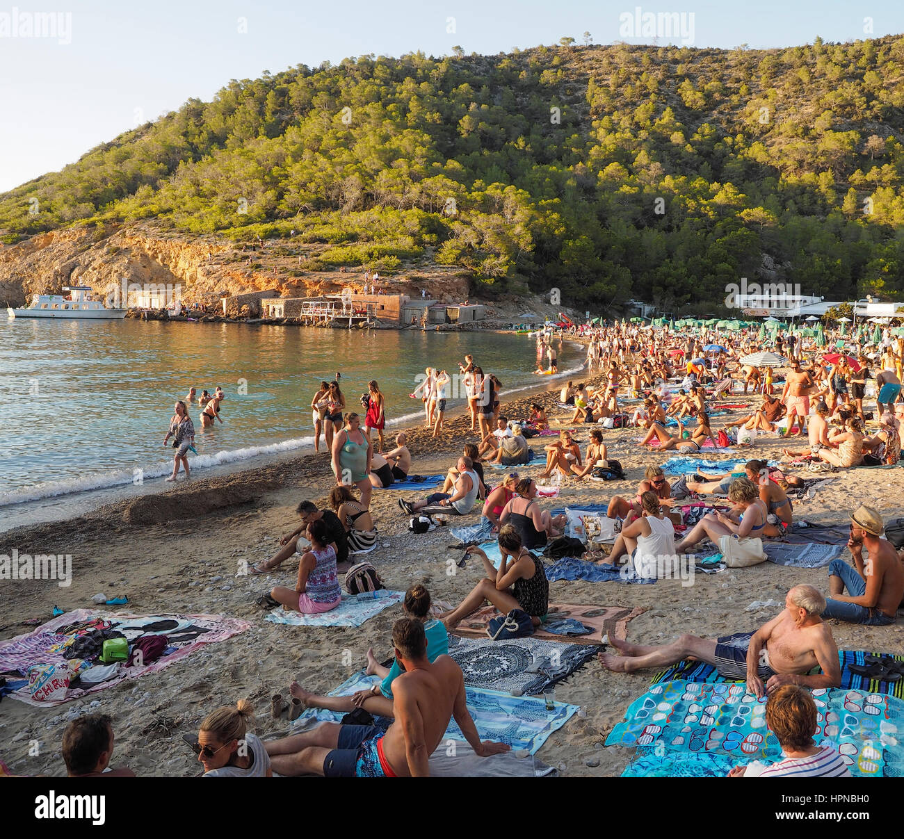 GATHERING OF VISITORS ON THE BEACH AT BENIRRAS BEACH IBIZA AND LISTENING TO DRUMS BEING PLAYED BY HIPPYS Stock Photo