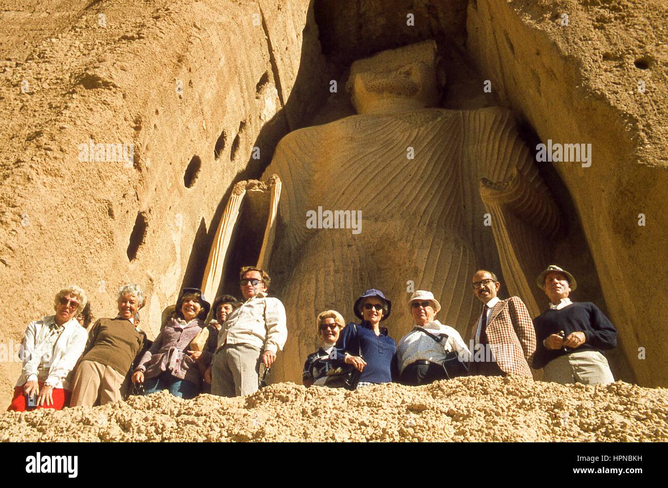 View of Western tourists posing before the massive height of the smaller giant Buddha, known as Shamama, in Bamiyan, Hazarajat region, central Afghanistan, November, 1975. Stock Photo