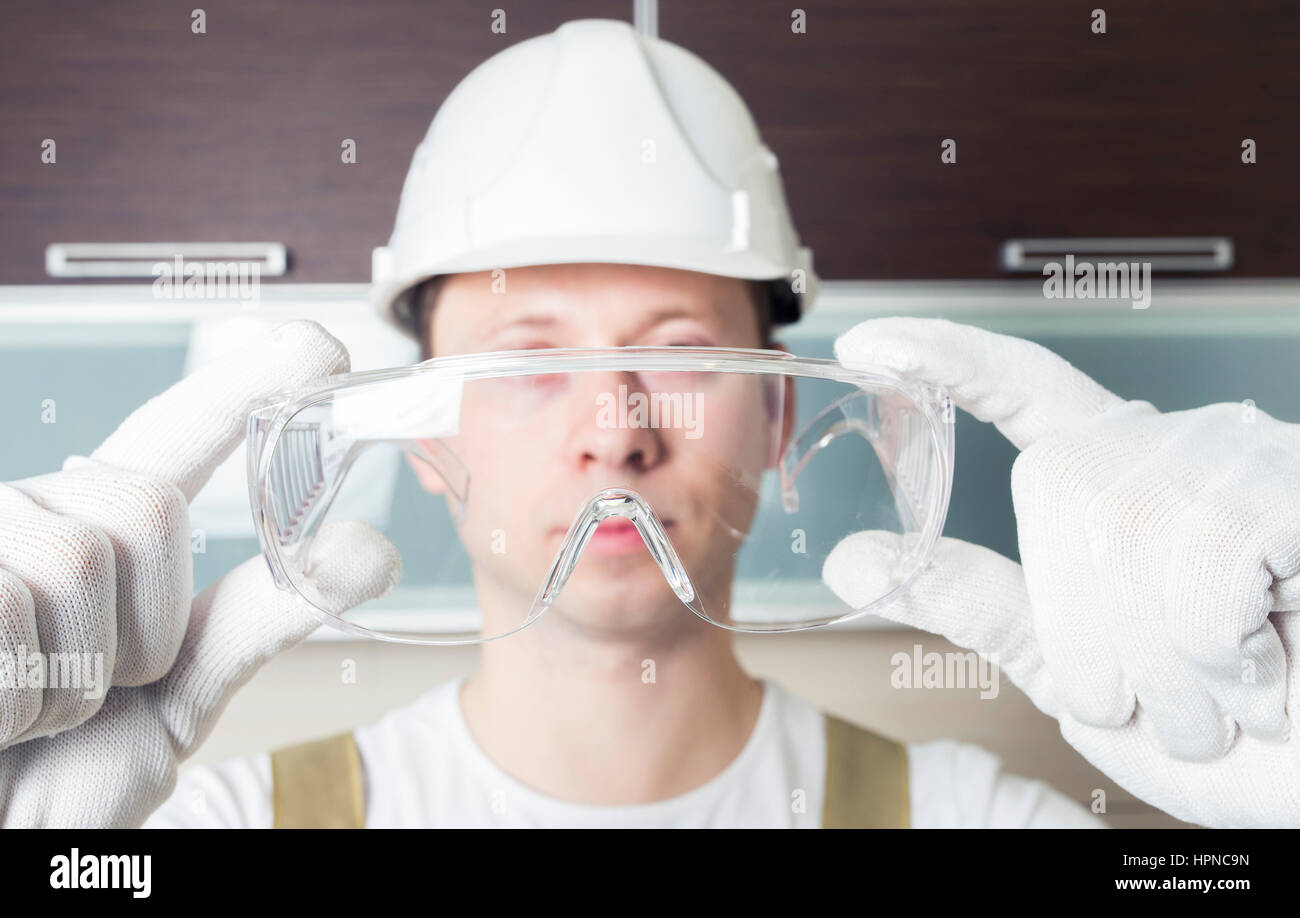 Worker holding transparent safety glasses. Head wearing white hard hat