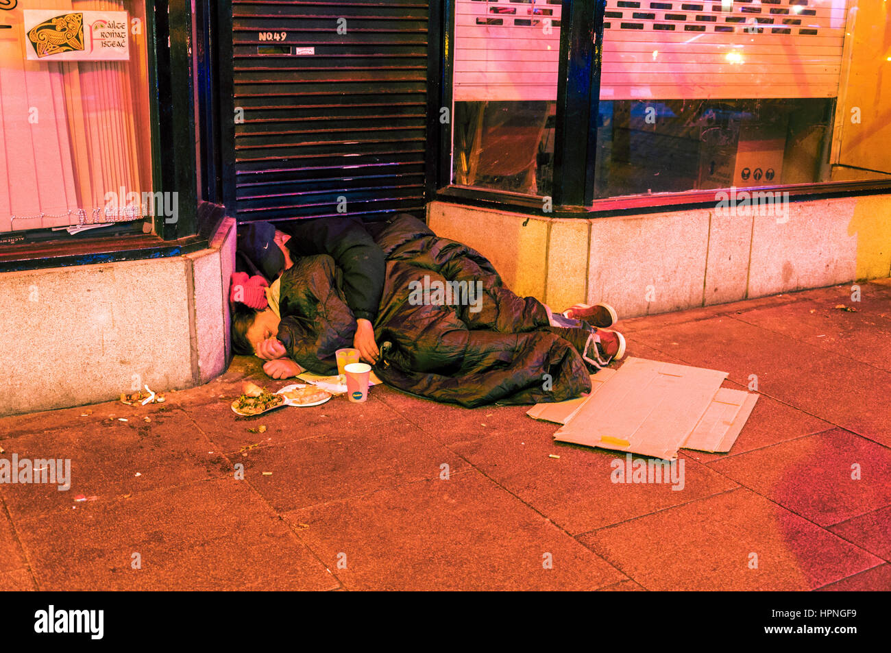 Homeless couple sleep in a doorway in Dublin, Ireland. Passers by have left some takaway food for them. Stock Photo
