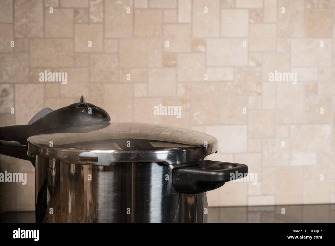 Stainless steel pressure cooker letting off steam on a modern induction cooking hob with glass top Stock Photo