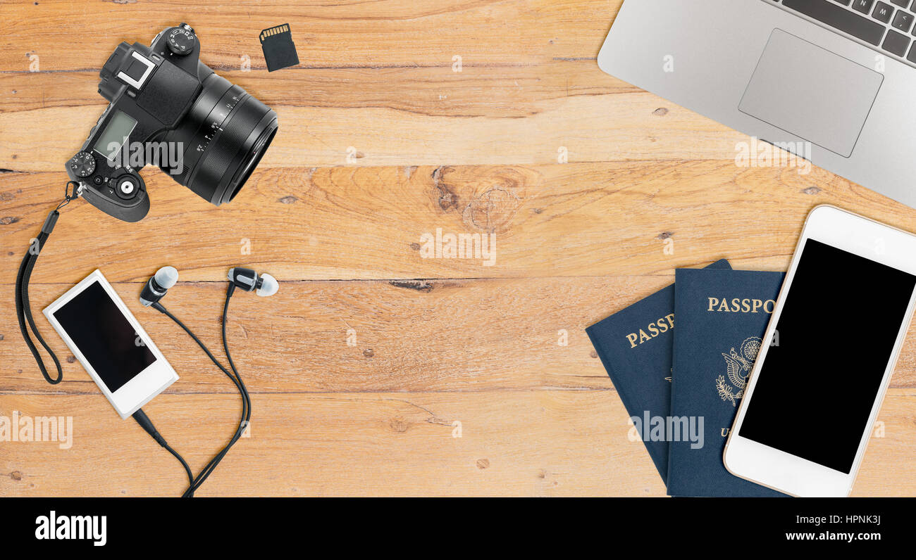 Clean and tidy wooden desk with equipment ready for travel including camera, laptop, phone, music player and passports Stock Photo