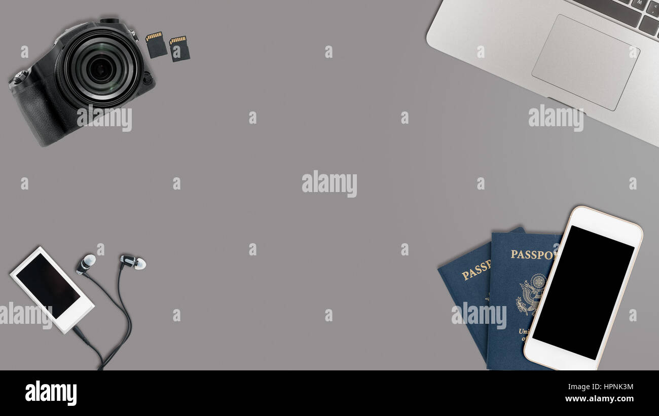 Clean and tidy grey desk with equipment ready for travel including camera, laptop, phone, music player and passports Stock Photo