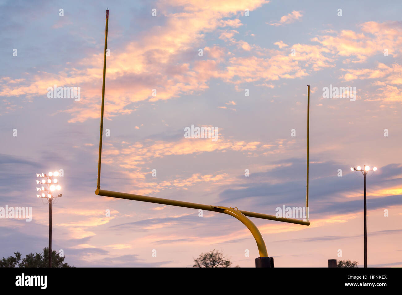 Yellow american football goal posts at school field against the lights and clouds of setting sun Stock Photo