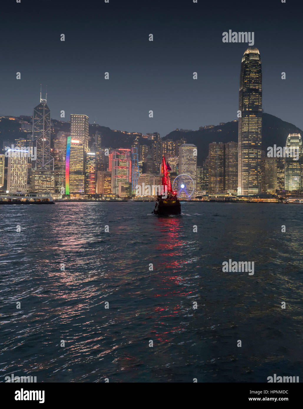 Old traditional Chinese ship with tourists sailing in the Victoria Harbour at night with the skyscrapers and the Hong Kong skyline. China. Stock Photo