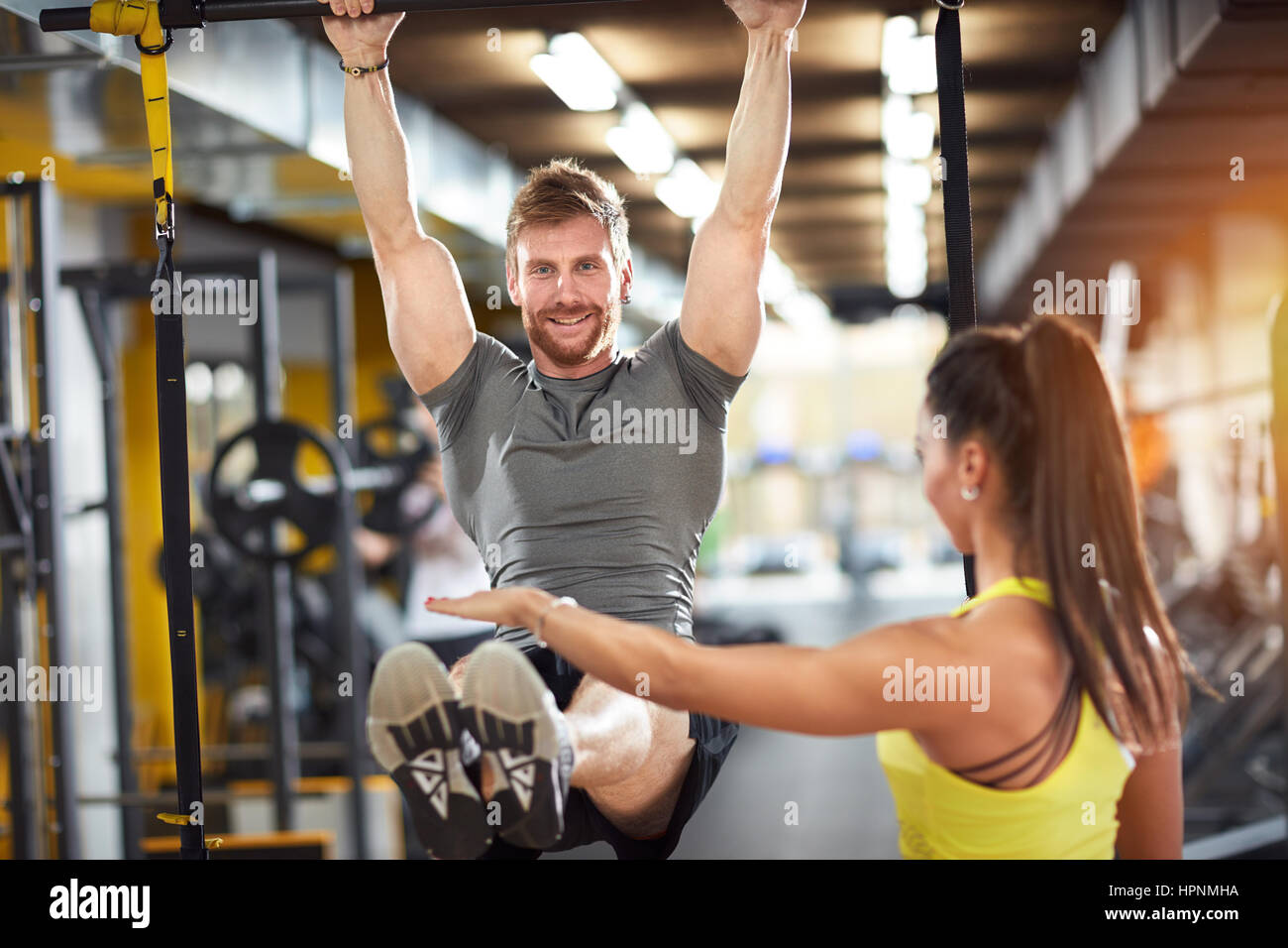 Male doing pull-up exercise with coach assisting in fitness club Stock Photo