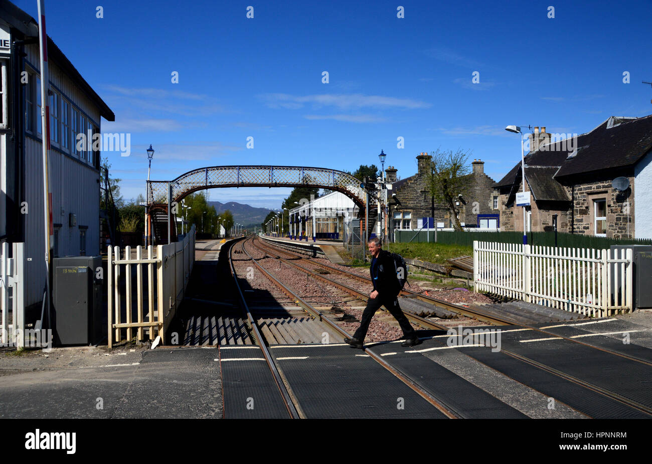 Male Hiker Walking Across the Level Crossing at Kingussie Train Station Speyside on the East Highland Way in the Scottish Highlands, Scotland, UK. Stock Photo