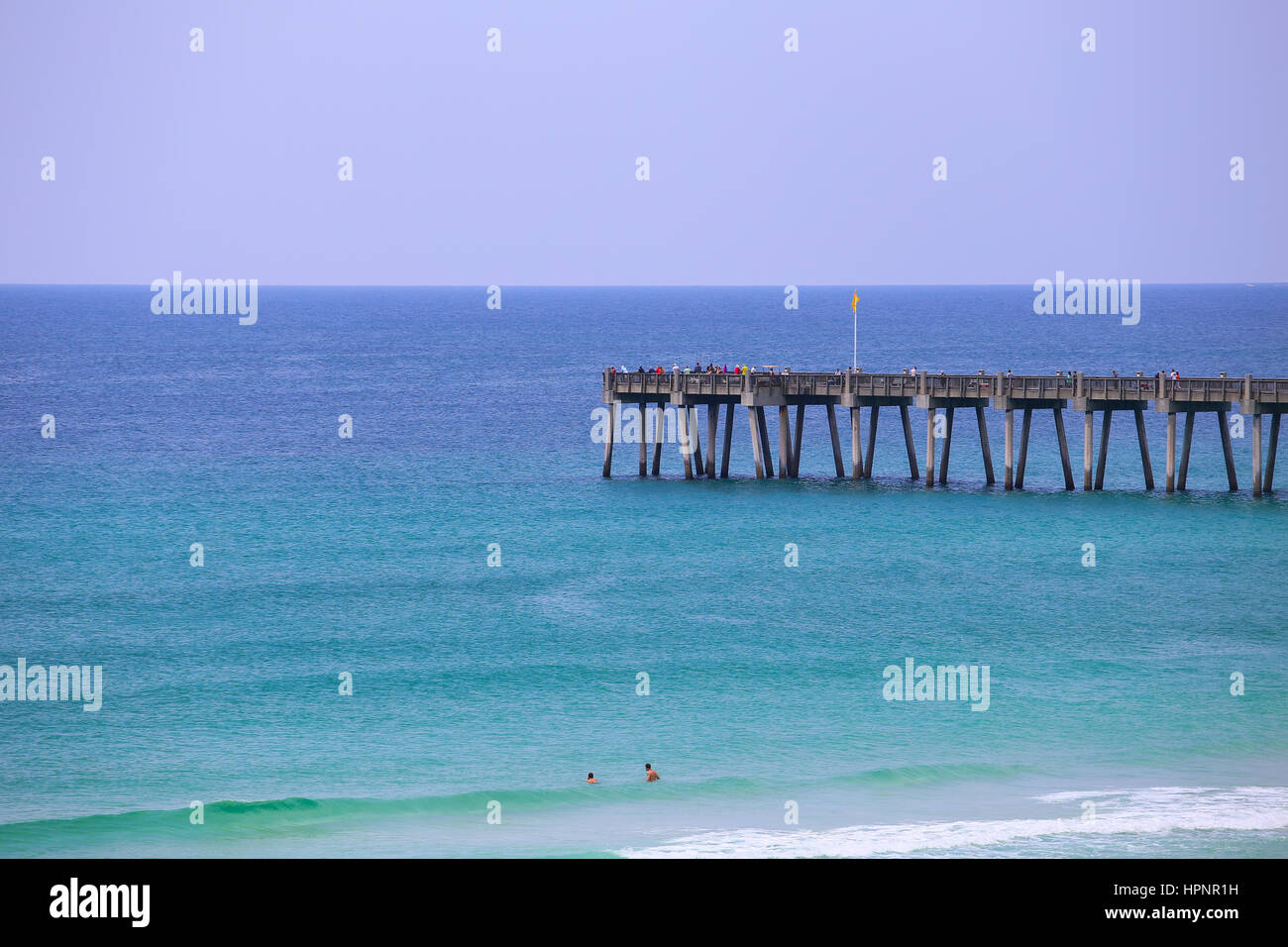 Pensacola Beach, USA - May 13, 2015: Looking from the beach towards Pensacola Beach Gulf Pier. There are people fishing on the pier and also some swim Stock Photo