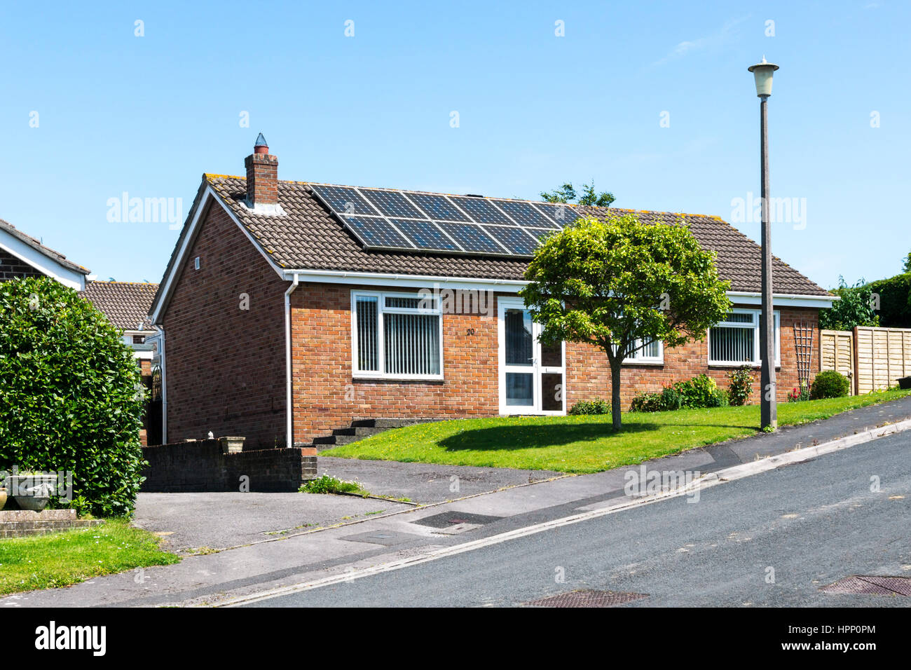 Solar panels on the roof of a small bungalow on a summer day with bright blue sky. Stock Photo