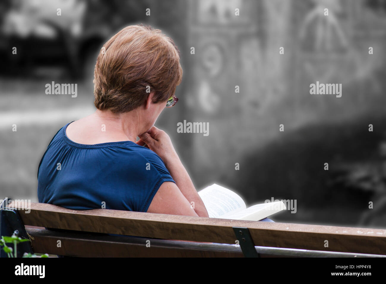 Woman reading a book while sitting on a bench Stock Photo - Alamy
