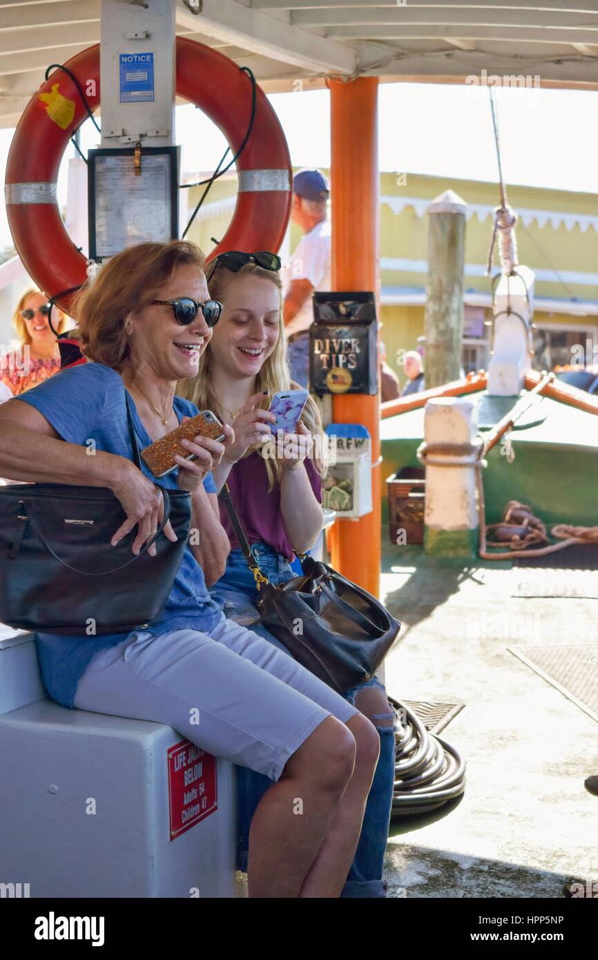 A mother and daughter laughing and smiling while using cell phones on a Florida tour boat with a life preserver in the backgrounjd Stock Photo