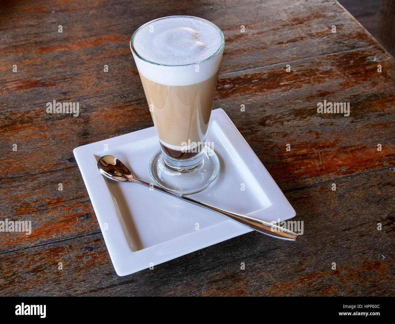Latte macchiato in a beautiful glass, a spoon and a white plate on a dark  wooden table Stock Photo - Alamy