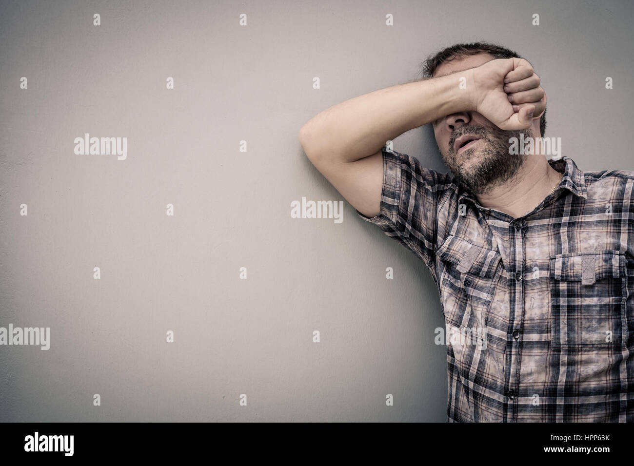 portrait one sad man standing near a wall and covers his face at the ...